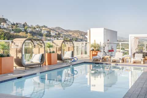 Modern pool deck with egg-shaped woven lounge chairs, white furniture, and hillside views