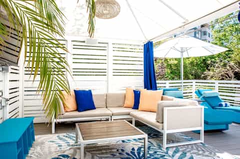 Modern rooftop lounge with beige sectional sofa, blue accents, and palm leaf decor