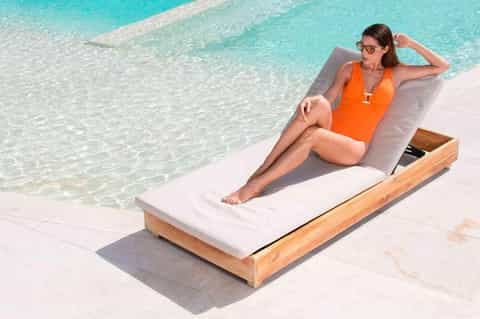Woman in orange swimsuit relaxing on cushioned lounge chair at tropical beachside pool