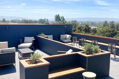 Contemporary rooftop terrace with dark blue walls, wooden planter boxes with greenery, lounge seating, and mountain views