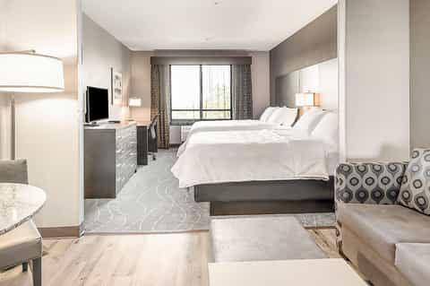 Contemporary hotel room with two queen beds, desk, flat-screen TV, and floor-to-ceiling windows