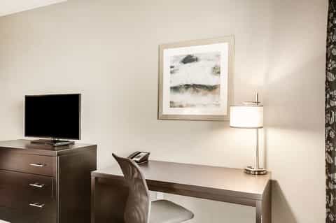 Modern hotel room desk with TV, lamp, and framed beach artwork on neutral walls