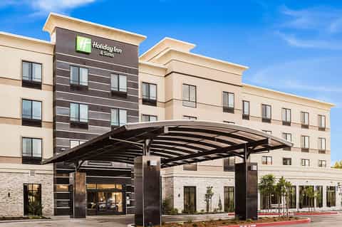 Holiday Inn & Suites hotel exterior with beige and dark facade under clear blue sky