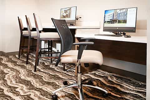 Contemporary business center with desktop computer, desk chairs, and zebra-patterned carpet in neutral office setting