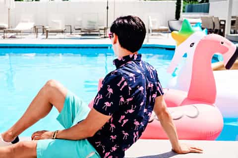Man relaxing poolside on inflatable unicorn float in swim trunks