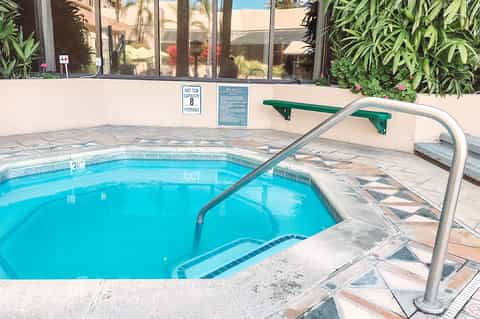 Spa hot tub with metal handrail and capacity sign, surrounded by desert landscape and modern building