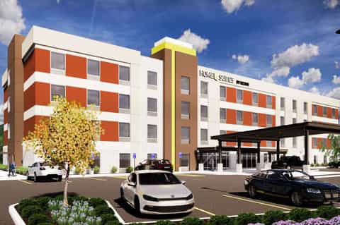 Home Suites hotel exterior rendering with orange and white brick facade, covered entrance, and parked vehicles