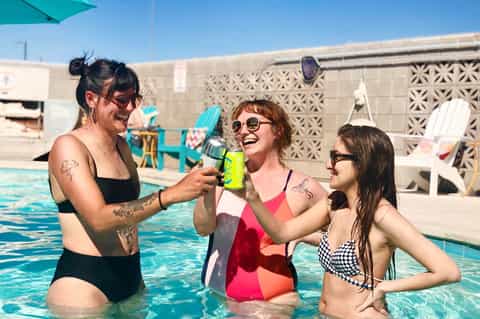 Three women in a pool holding colorful beverages and smiling in the sunshine