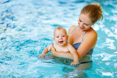 Woman and baby enjoying shallow pool water together, smiling