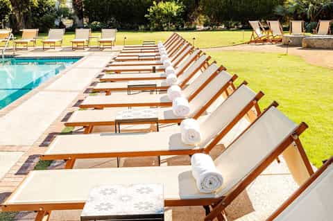 Row of wooden lounge chairs with white towels by a rectangular pool and manicured lawn