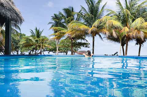 Infinity pool with palm trees reflecting in clear turquoise water with beachfront views