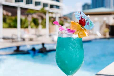 Tropical turquoise cocktail with umbrella and cherry by resort pool