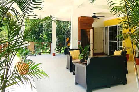 Covered outdoor patio with tropical plants, casual seating, and ceiling fan