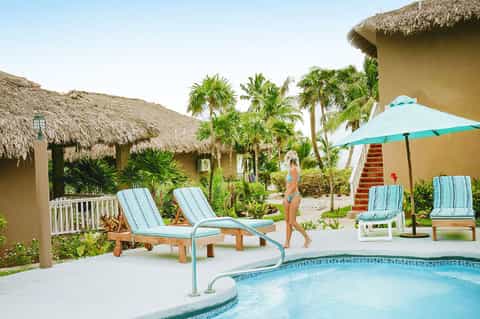 Resort pool area with thatched-roof structures, lounge chairs, and palm trees surrounding the water