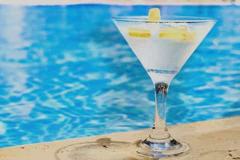 Cocktail with pineapple garnish at poolside with blue water background