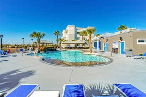 Resort pool area with circular design, palm trees, lounge chairs, and modern white building