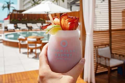 Tropical cocktail with fruit garnish held at resort poolside with lounge chairs visible