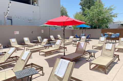 Outdoor deck with tan lounge chairs under red and blue umbrellas beside concrete wall