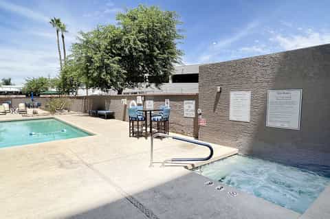 Desert resort pool area with spa tub, lounge chairs, concrete wall with rules signage, and palm trees