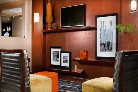 Modern hotel lounge with rust-orange walls, flat-screen TV, artwork, and contemporary furnishings