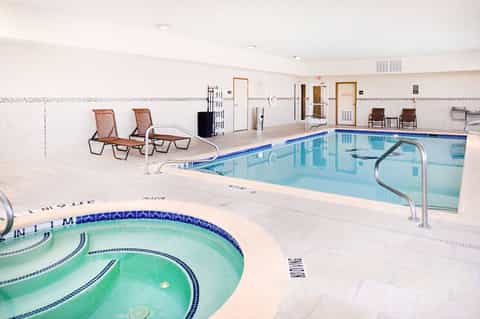 Indoor pool facility with spa tub and lounge chairs in bright, clean recreation area