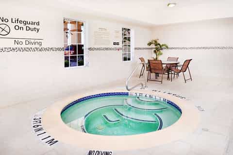 Indoor circular hot tub with turquoise water in bright room with tile walls and safety signage