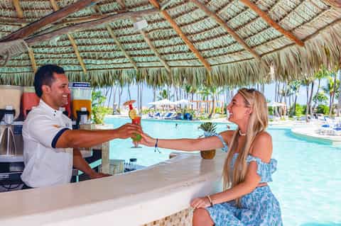 Bartender serving tropical drink to woman at tiki bar overlooking resort pool