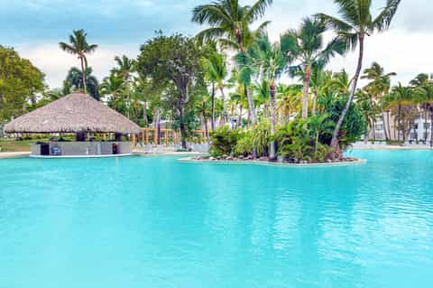 Lagoon-style pool with thatched bar and palm trees in resort courtyard