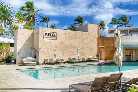 Contemporary resort pool with turquoise water, P.B.G. beach club building, palm trees, and loungers