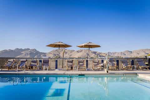 Resort pool with lounge chairs and umbrellas overlooking desert mountains under clear blue sky