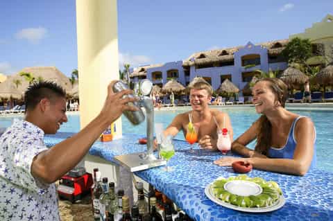 Bartender photographing guests at swim-up pool bar with tropical resort backdrop