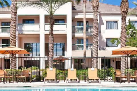 Modern resort building with palm trees, lounge chairs, and orange umbrellas by pool