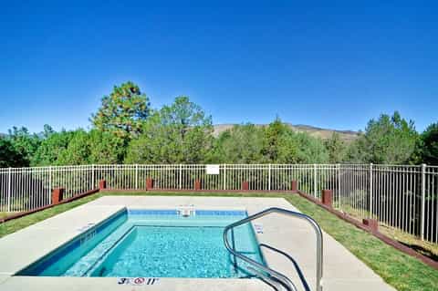 Outdoor swimming pool with white safety railing surrounded by green trees and mountains