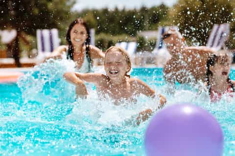 Children playing and splashing in bright turquoise pool with adults supervising