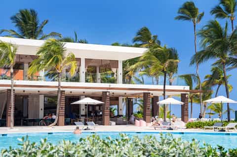 Modern pool area with white cabana structure, palm trees, lounge chairs, and ocean backdrop