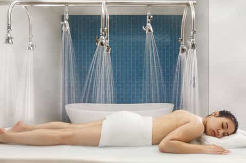 Spa treatment area with rainfall showerheads and tiled accent wall behind a white soaking tub
