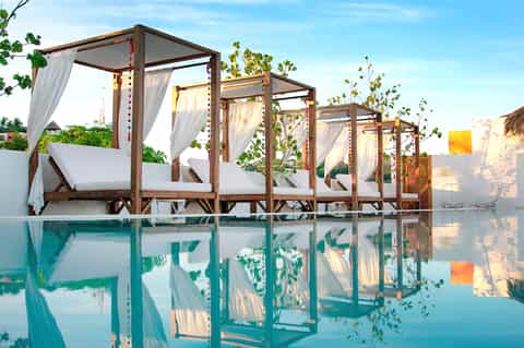 Luxury resort pool cabanas with white curtains reflected in turquoise water at sunset