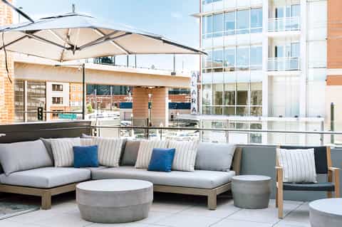 Rooftop lounge with gray sectional sofa, striped pillows, umbrellas, and waterfront skyline views