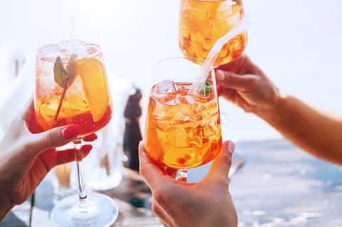 Hands holding tropical cocktails with ice and garnish against ocean and sky background
