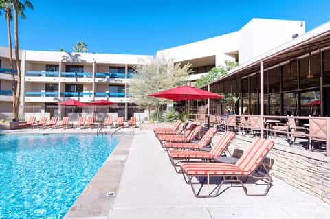 Resort pool area with red umbrellas, striped lounge chairs, and mid-century modern white building