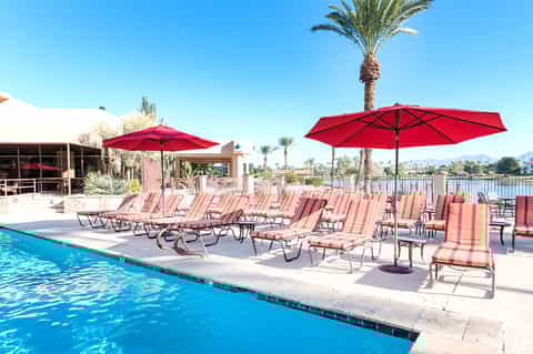 Resort poolside with red striped lounge chairs under red umbrellas and palm trees