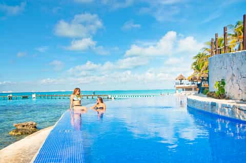 Infinity pool blending into ocean at tropical resort with palm trees and clear water