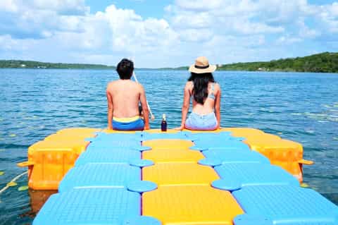 Two people sitting on colorful modular floating dock on lake with forest backdrop