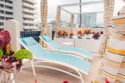 Rooftop terrace with turquoise lounge chairs, striped umbrellas, and city skyline views
