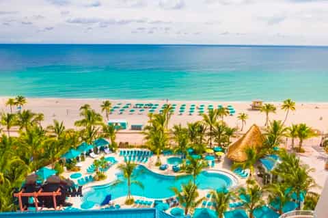Aerial view of beachfront resort with turquoise pools, palm trees, and ocean