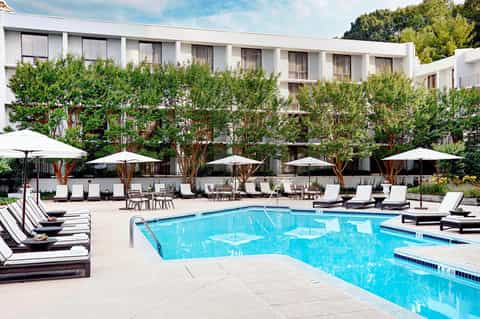 Resort pool with lounge chairs, white umbrellas, and ivy-covered building backdrop