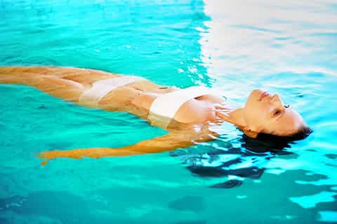 Woman floating peacefully in bright turquoise pool water