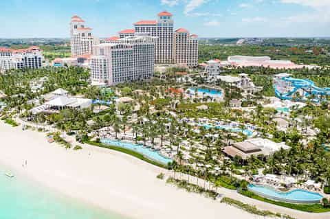 Aerial view of beachfront resort with pink buildings, pools, white sand beach, and palm trees