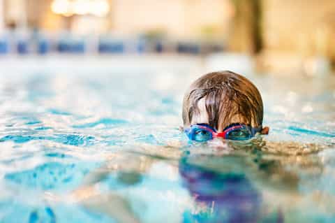 Child swimming in indoor pool wearing blue and red goggles