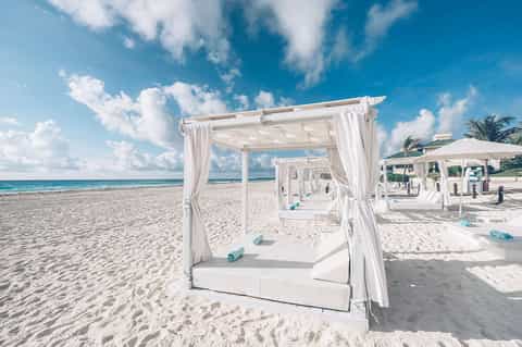 White cabanas with flowing curtains on pristine beach with turquoise ocean and palm trees